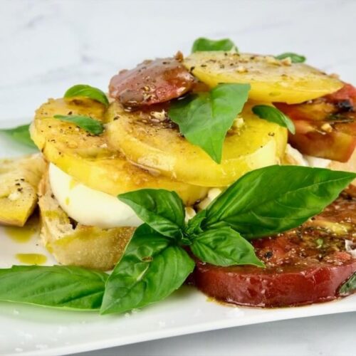 Marinated tomatoes layered on a plate with burrata cheese and fresh basil
