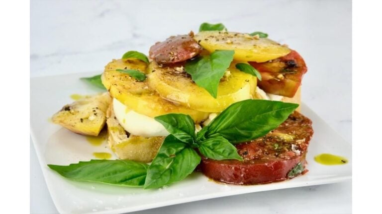 Marinated tomatoes layered on a plate with burrata cheese and fresh basil
