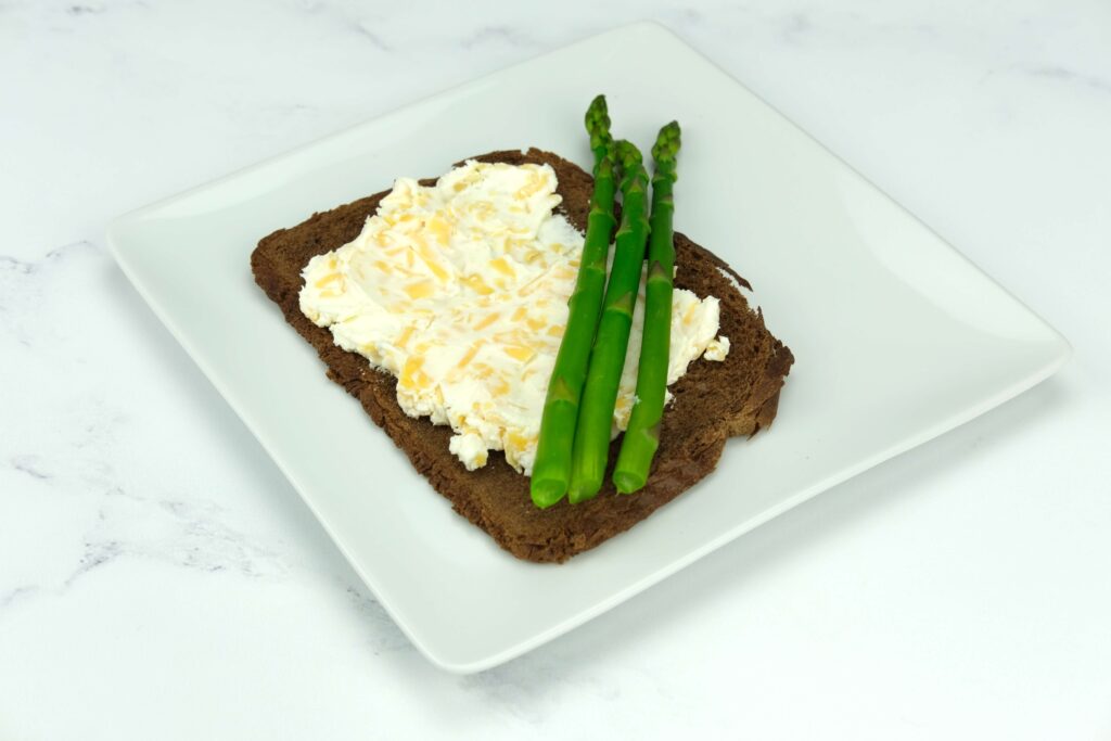pumpernickel bread with cream cheese and cheddar cheese prepared for rolling with pre-prepared asparagus