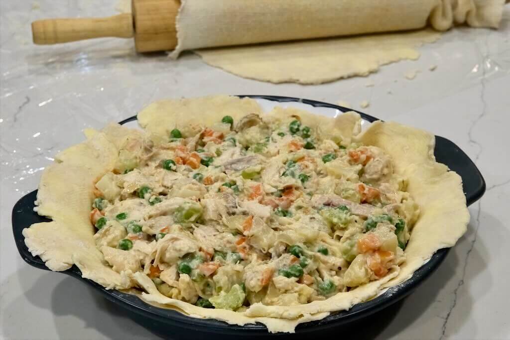 rolled out flaky crust dough on a pie pan with chicken filling