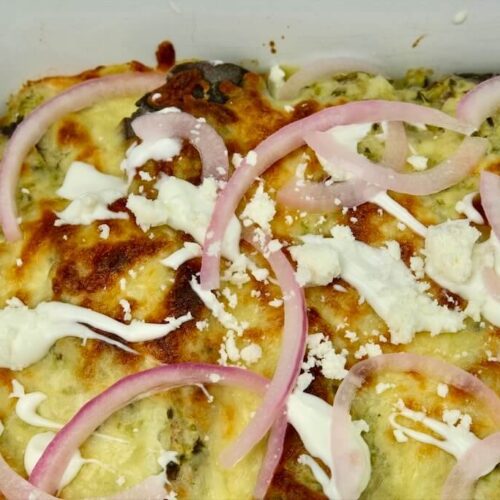 baked enchiladas suizas with crema and sprinkled with Cotija cheese, iceberg lettuce, and pickled onions