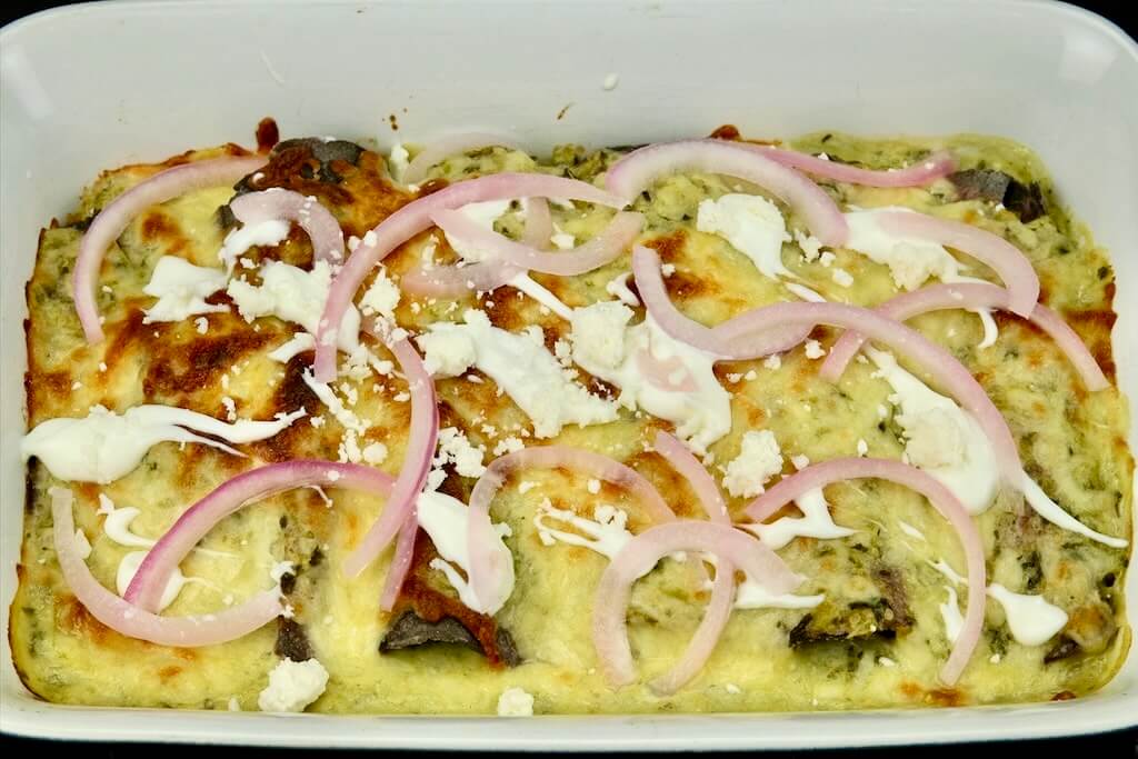 baked enchiladas suizas with crema and sprinkled with Cotija cheese, iceberg lettuce, and pickled onions