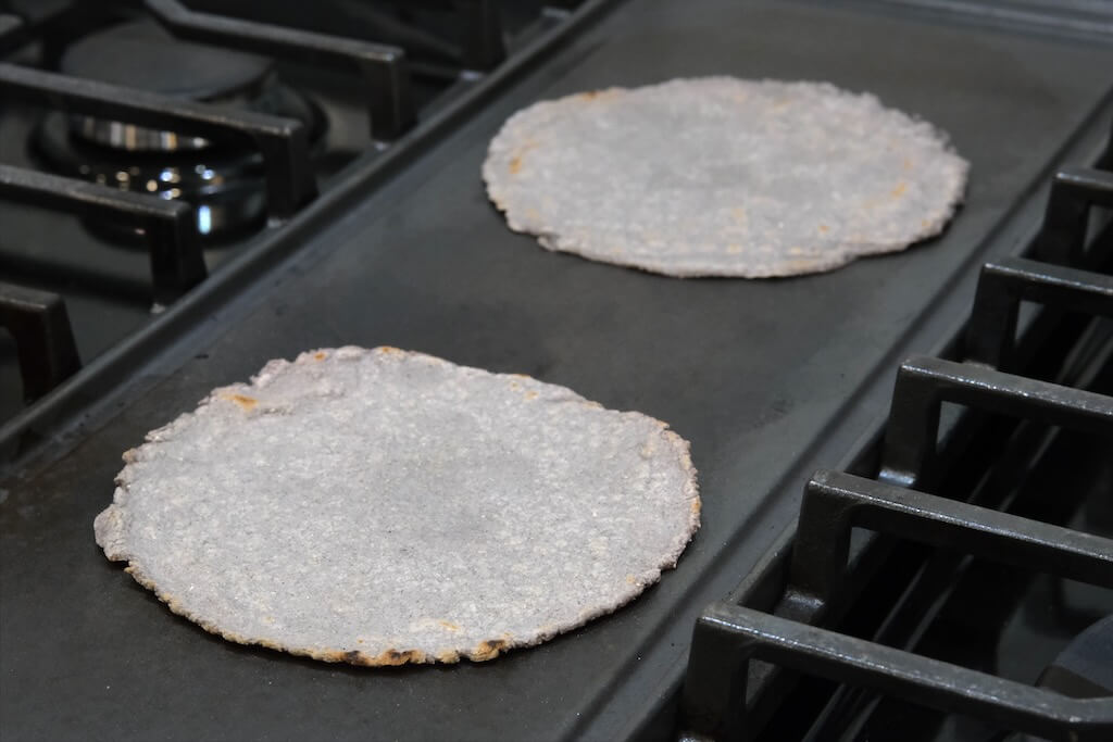 homemade corn tortillas cooking in a hot griddle or cast-iron pan