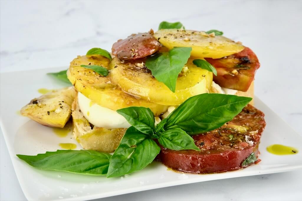 Marinated tomatoes layered on a plate with burrata cheese and fresh basil