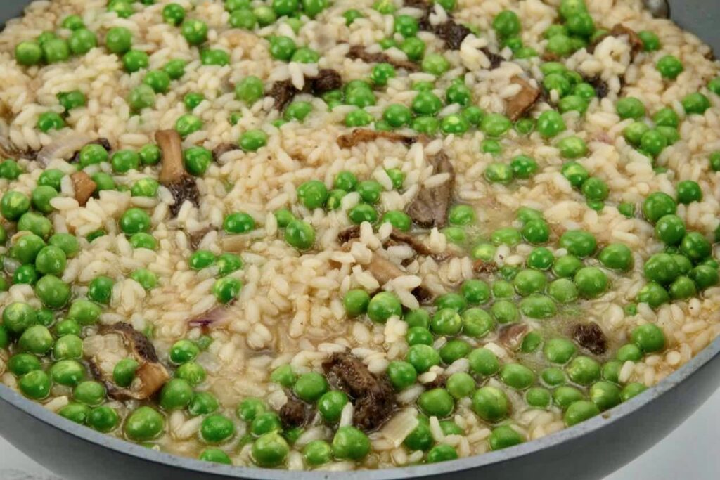 a pan of arborio rice with morel mushroom, English peas, and ramps simmering in stock