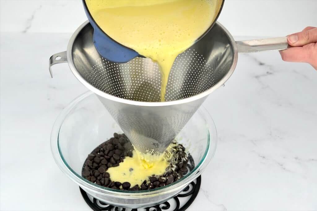 thickened egg yolk mixture being poured into a bowl of dark chocolate
