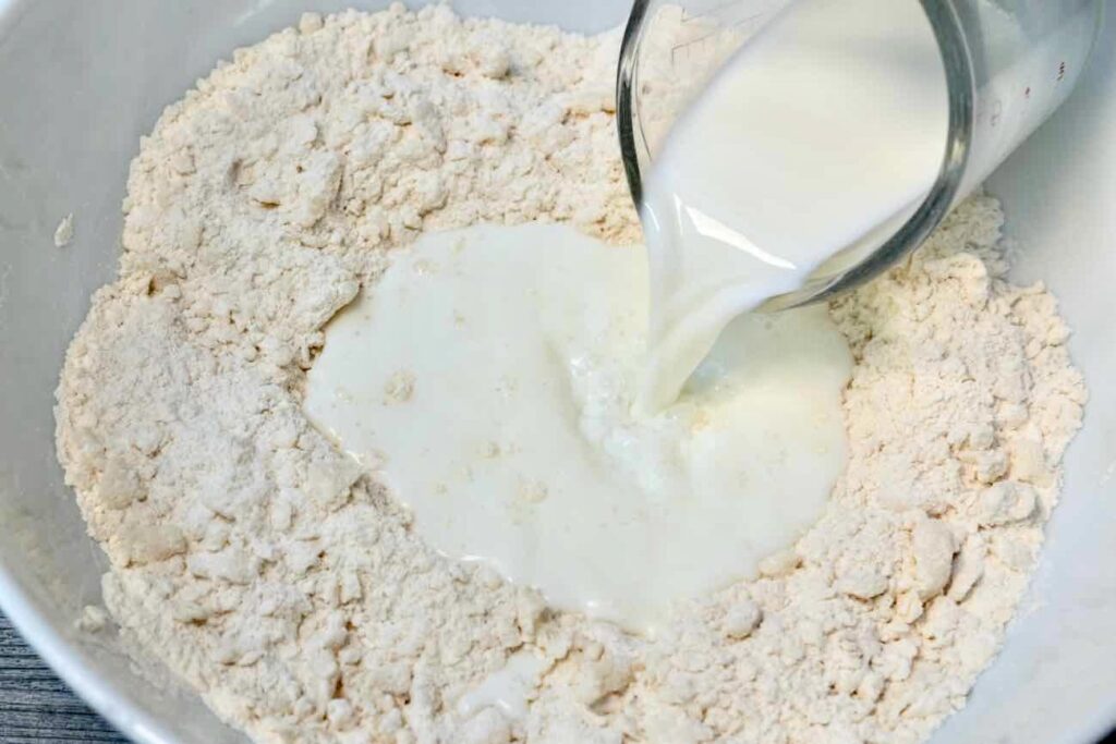 Milk being poured in a mixture of flour, baking powder, sugar, and salt with coconut oit for vegan sweet biscuits