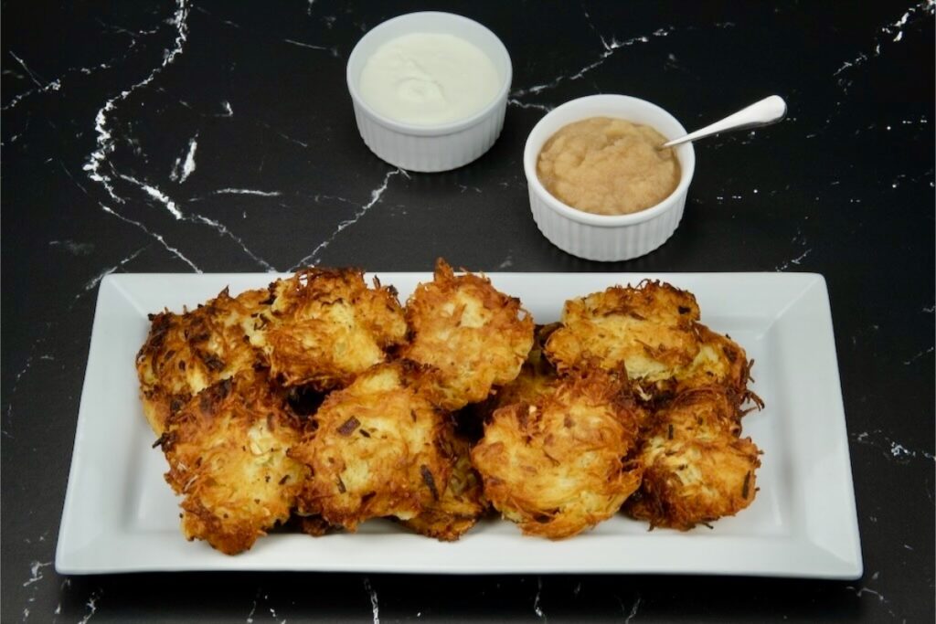 a serving of crispy golden latkes served with applesauce and sour cream