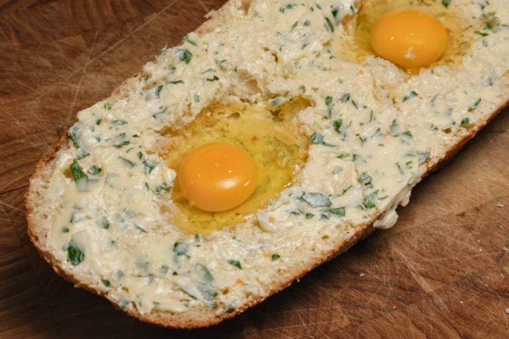 bread with garlic butter and holes with raw eggs