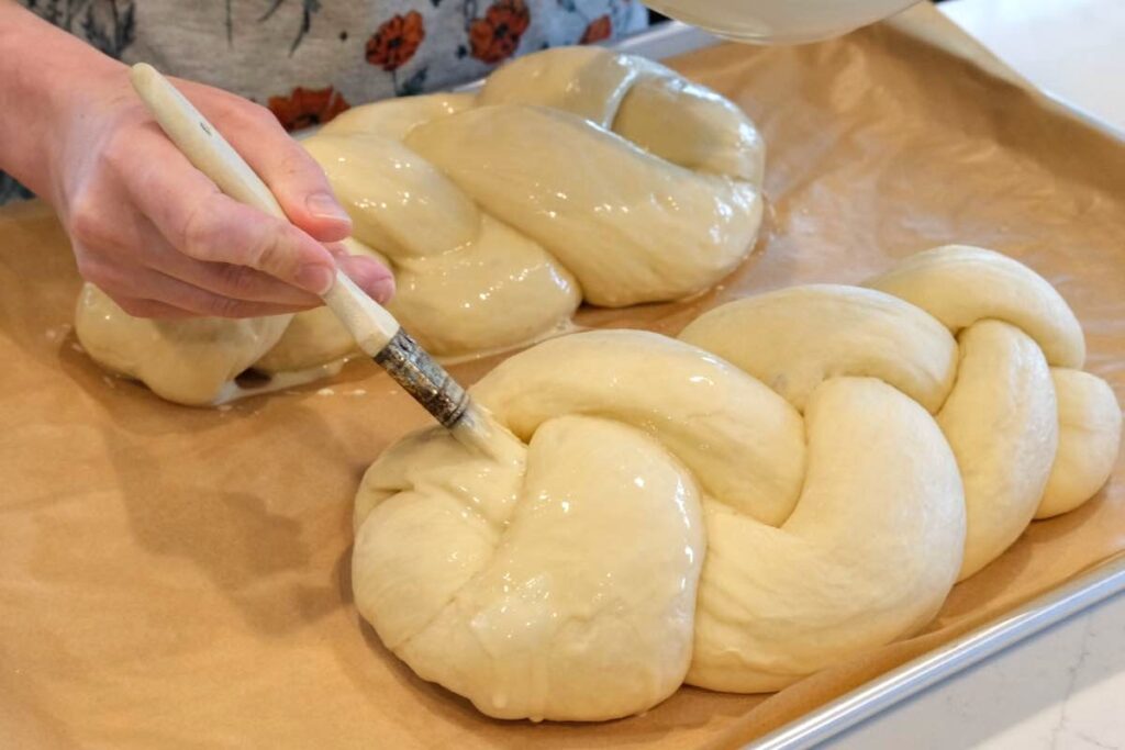 brushing eggwash to beautifully braided homemade challah bread dough